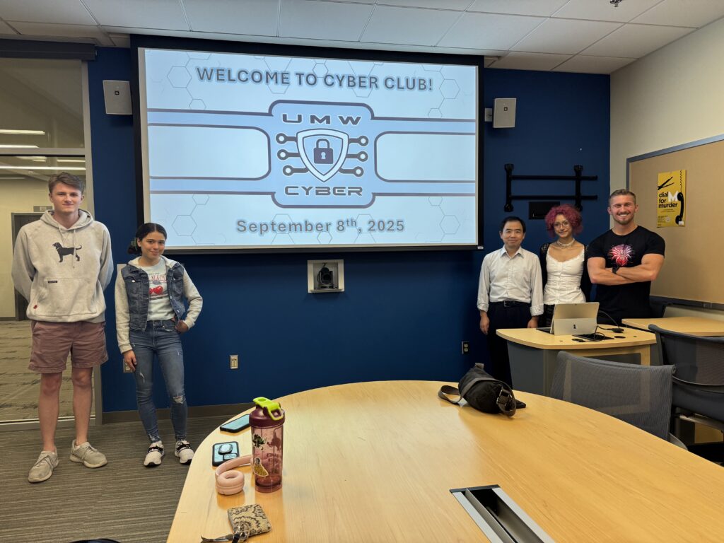 Five members of the UMW Cyber Club standing at the front of a meeting room. The presenting screen says "Welcome to Cyber Club! September 8th, 2025" behind them.